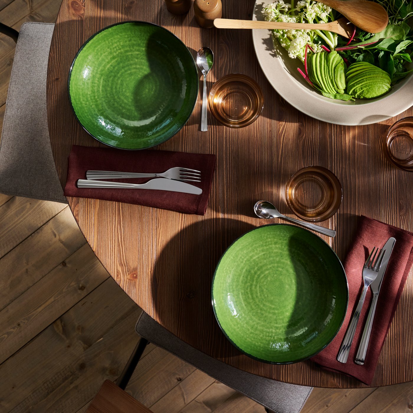 A wooden dining table with PELARKAKTUS side plates in green, set alongside cutlery, napkins, glasses and salad bowl.