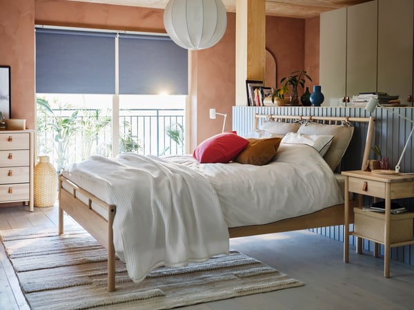 Ein Schlafzimmer in Beige und Grau mit BJÖRKSNÄS Bettgestell, Ablagetischen und Kommoden mit 5 Schubladen aus massiver Birke