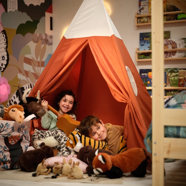 Two children in a HÖVLIG tent play with all the ALPTALL soft toys, including the Bengal tiger and red panda.
