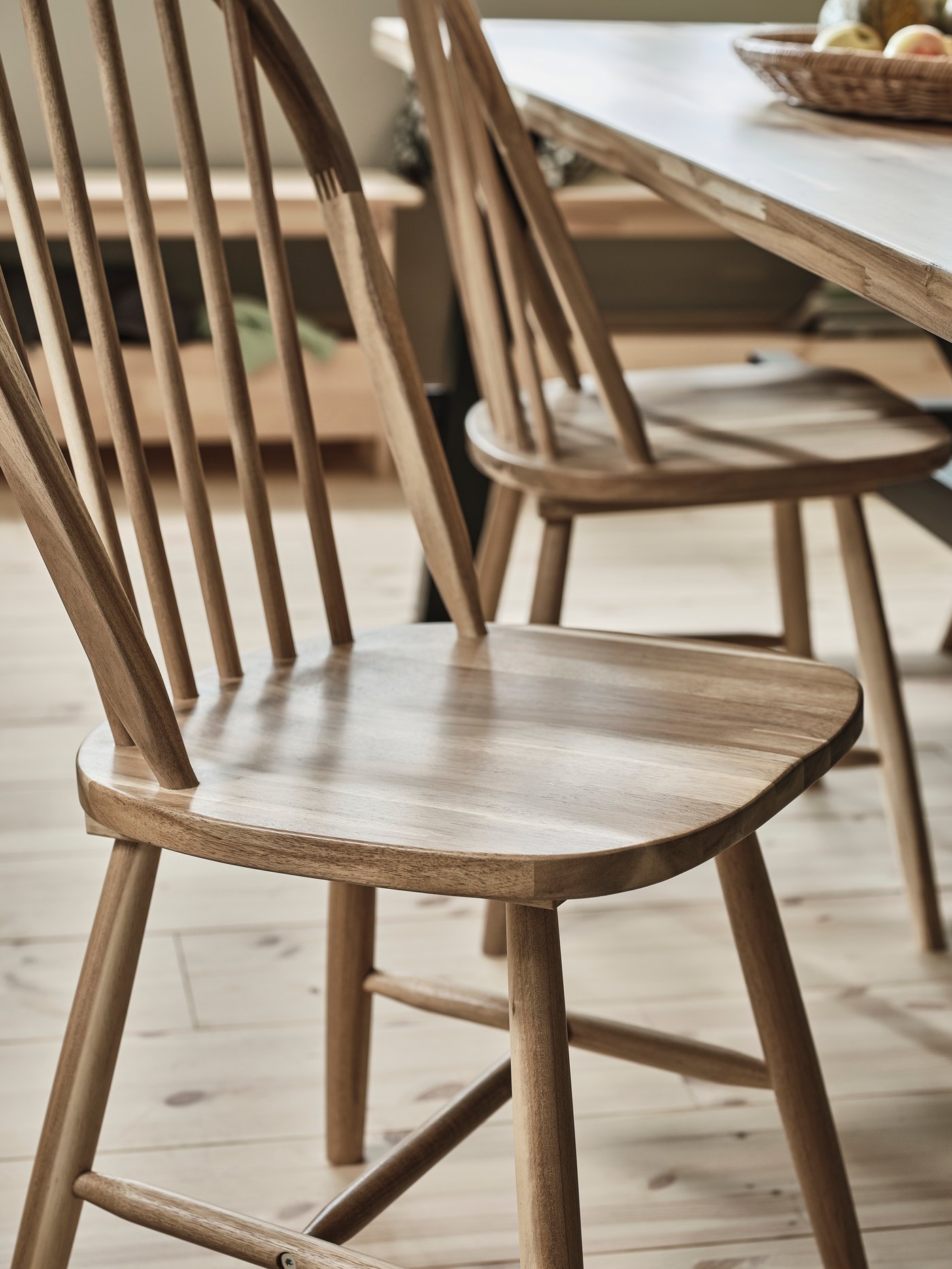 Dans une salle à manger baignée de lumière, deux chaises en bois SKOGSTA en acacia massif sans coussins près d’une table de salle à manger SKOGSTA.