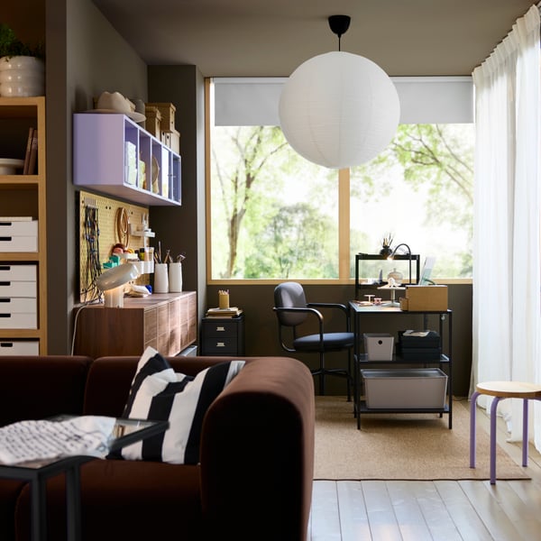 A shared dedicated workspace setup with a black-brown VITTSJÖ desk featuring a glass top, a chair, storage boxes, and a lamp.