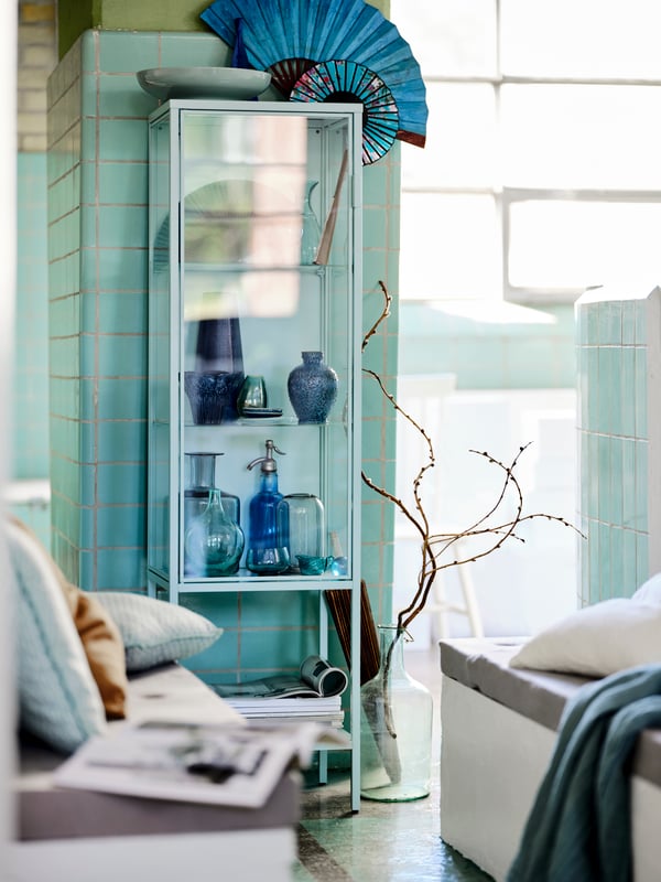 Armários BESTÅ com portas de diferentes cores fixados a uma parede perto de uma mesa LISABO em preto com velas em cima.