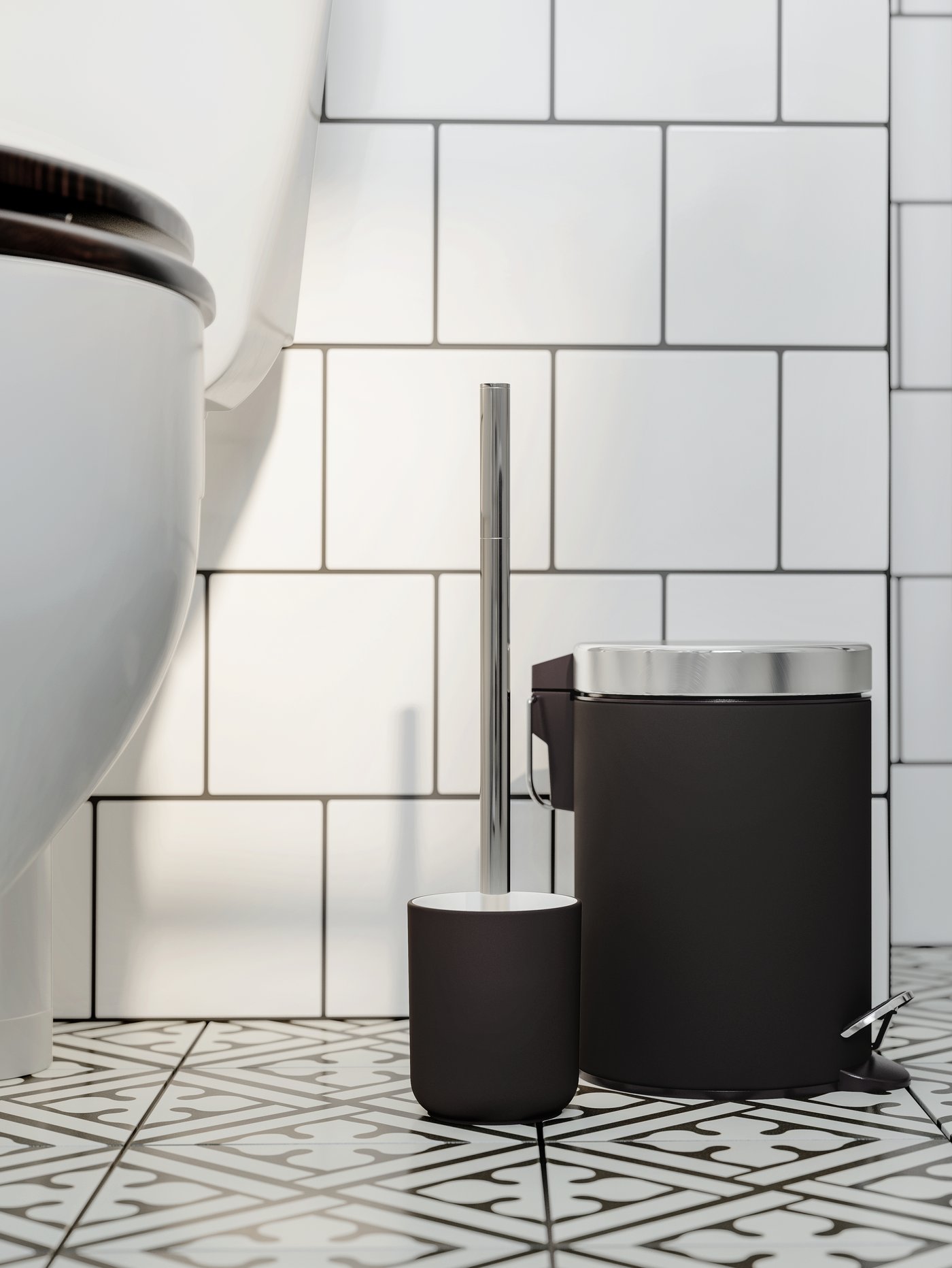 Cuarto de baño con paredes de azulejos y una escobilla gris junto a un cubo de basura redondo. Hay un inodoro blanco a un lado.