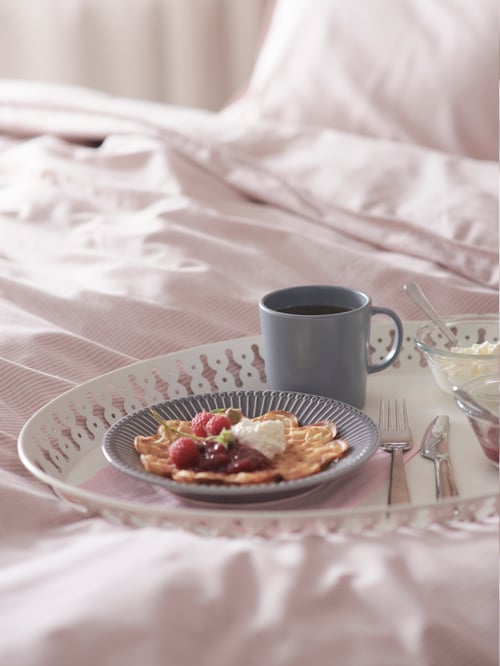 Dormitor cu cadru de pat, set de lenjerie de pat, tavă albă, un platou de servit cu mâncare, o cană cu cafea, un șervețel de hârtie, tacâmuri, bol.