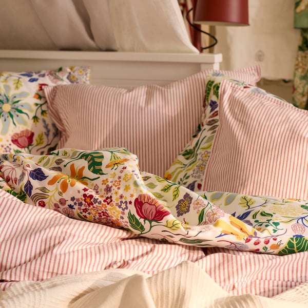 A close-up of a HEMNES daybed with a mix of bedlinen; the striped SOLFIBBLA and the floral patterned BRUDKRUSBÄR.