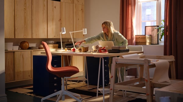 A room where a woman reaches over an arrangement of desk spaces flanked by HELMER drawer units and a wall of IVAR cabinets.