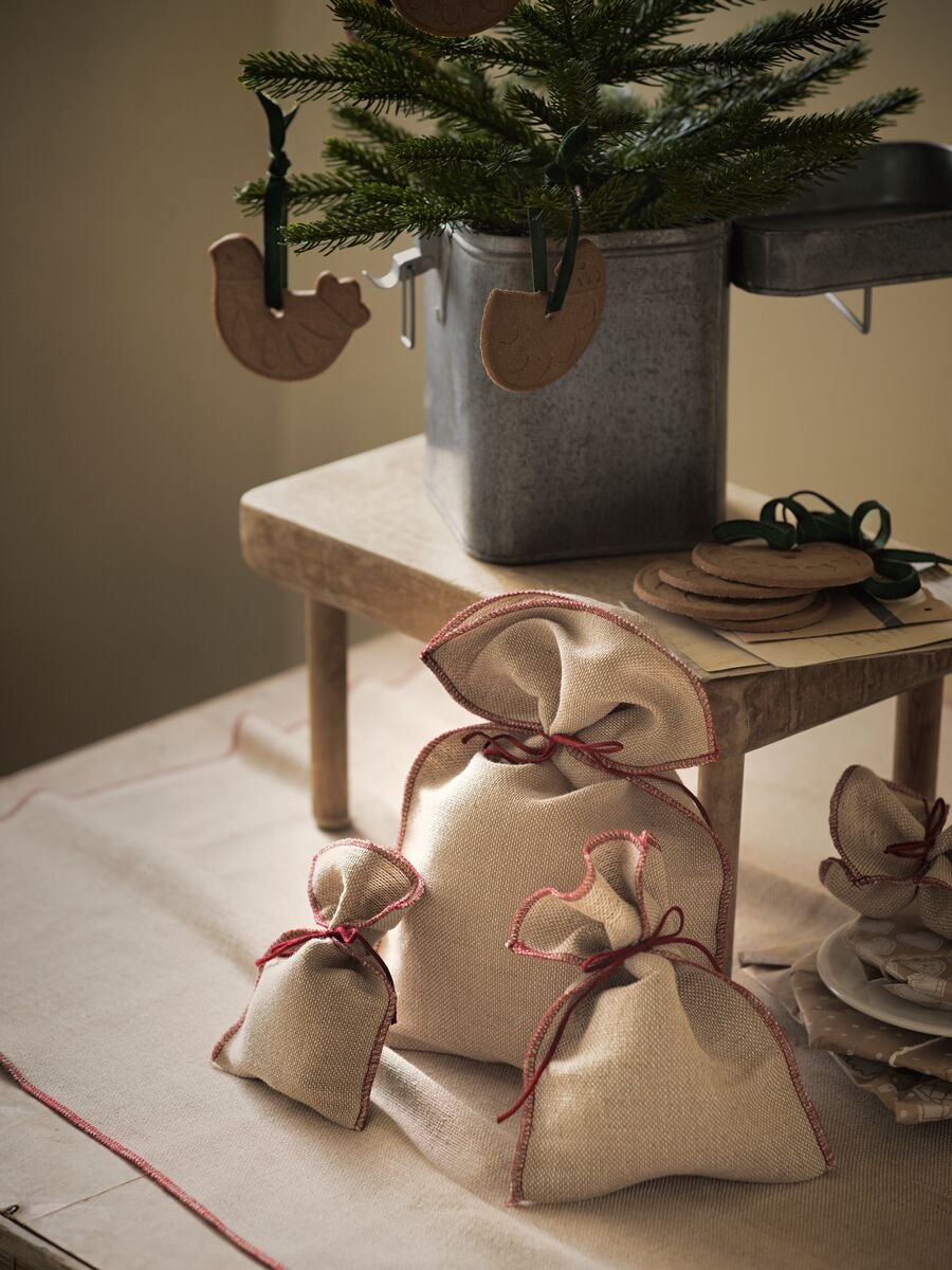 Několik dárků zabalených v jutovém balicím papíru VINTER 2020 leží pod malou borovicí ozdobenou dřevěnými ozdobami ve tvaru zvířátek.