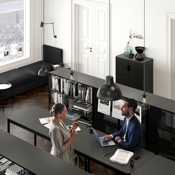 An office setting where a woman talks to a man in a suit who sits with his laptop by a TOMMARYD table.