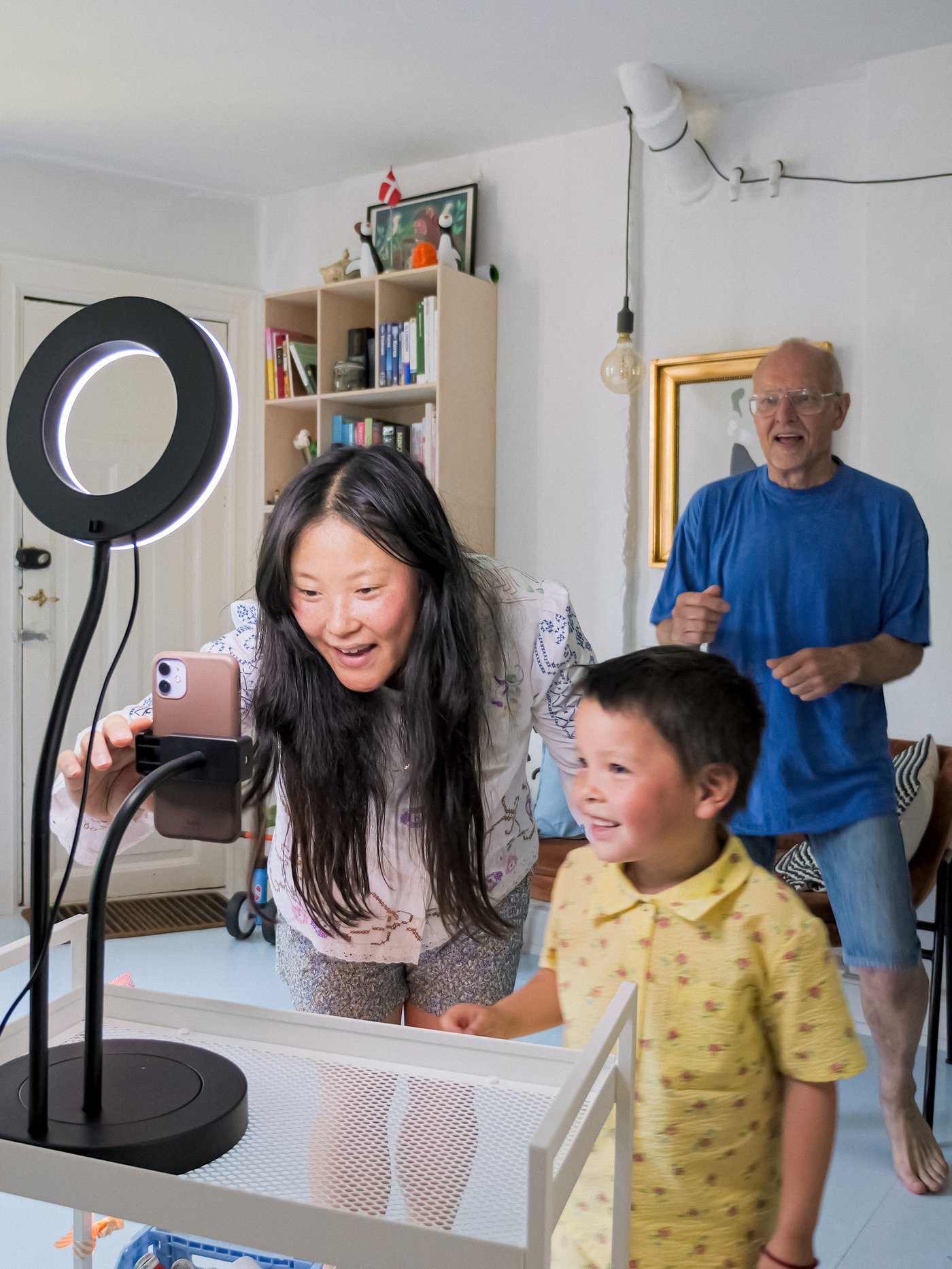 Une mère et son enfant installent un anneau lumineux avec support à téléphone LÅNESPELARE pour enregistrer une vidéo. Le père danse derrière eux.