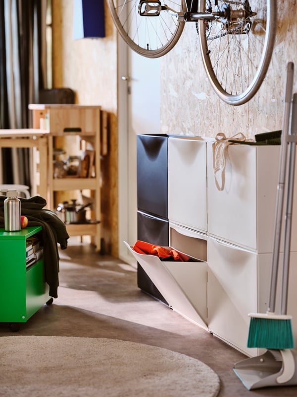Two white TRONES shoe cabinets with storage with one drawer open next to a black TRONES shoe cabinet with storage on a wall.