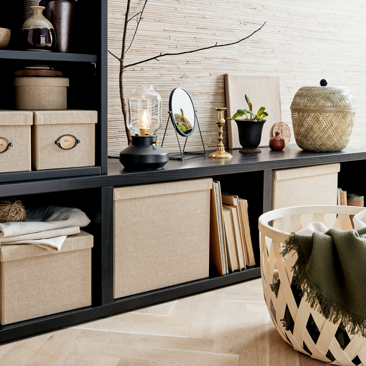 Černá sestava otevřených polic KALLAX na zemi, s knížkami a krabicemi uvnitř. Na sestavě jsou dekorace a rostliny.