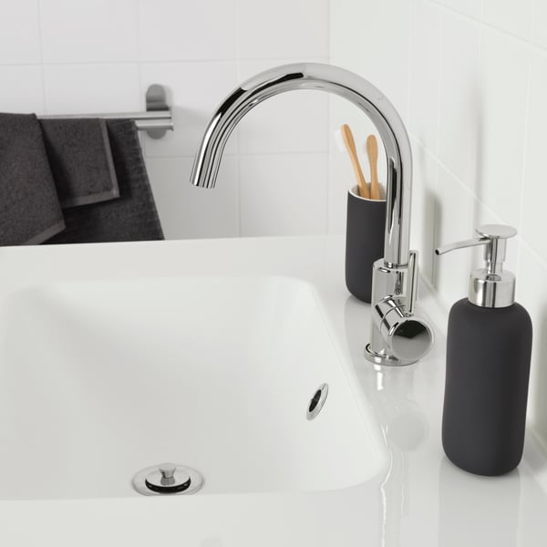 A close-up view of a modern bathroom sink with a sleek black faucet. The focus is on the clean lines and minimalist design, highlighting the simplicity and elegance of the fixture against the white basin and tiled background.