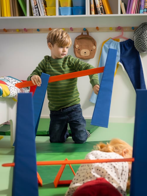 ベビールーム＆子ども部屋で、ブルーのSKRATTMÅS スクラットモス障害物コースで遊んでいる人がいる。横にはPLUFSIG ペルフスィッグ折りたたみ式ジムマット2枚。
