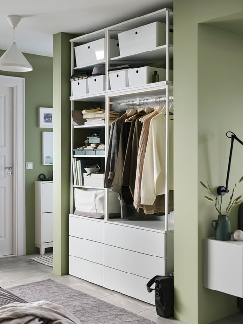 An open PLATSA wardrobe with drawers and hanging rail in a green and white hallway, holding boxes, objects, and clothing.
