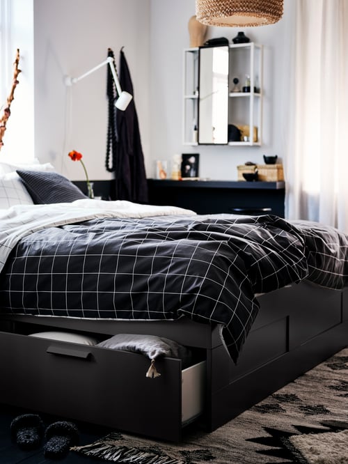 Bedroom with a bed frame with storage, a striped duvet cover with pillows, a mirror cabinet,  a work wall lamp, and a rug.