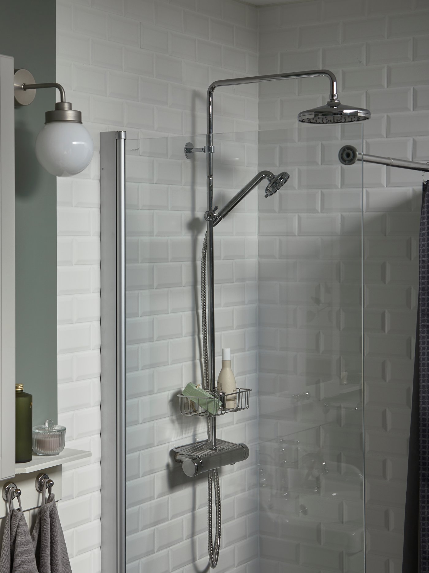 Bathroom with a grey shower shelf placed below a shower set with thermostatic mixer. A grey wall lamp is to the side.