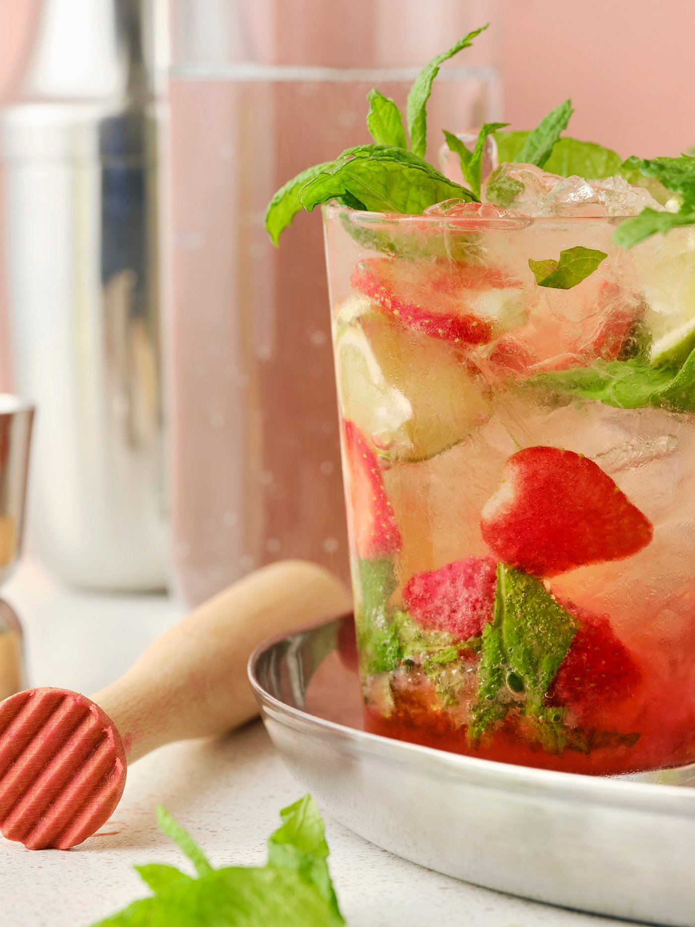 Es sind Gläser mit ISKUB Sprudelgetränk mit Zitronen-/Limettengeschmack, Erdbeeren und Minze zu sehen, serviert auf einem silberfarbenen Tablett mit Cocktailutensilien.