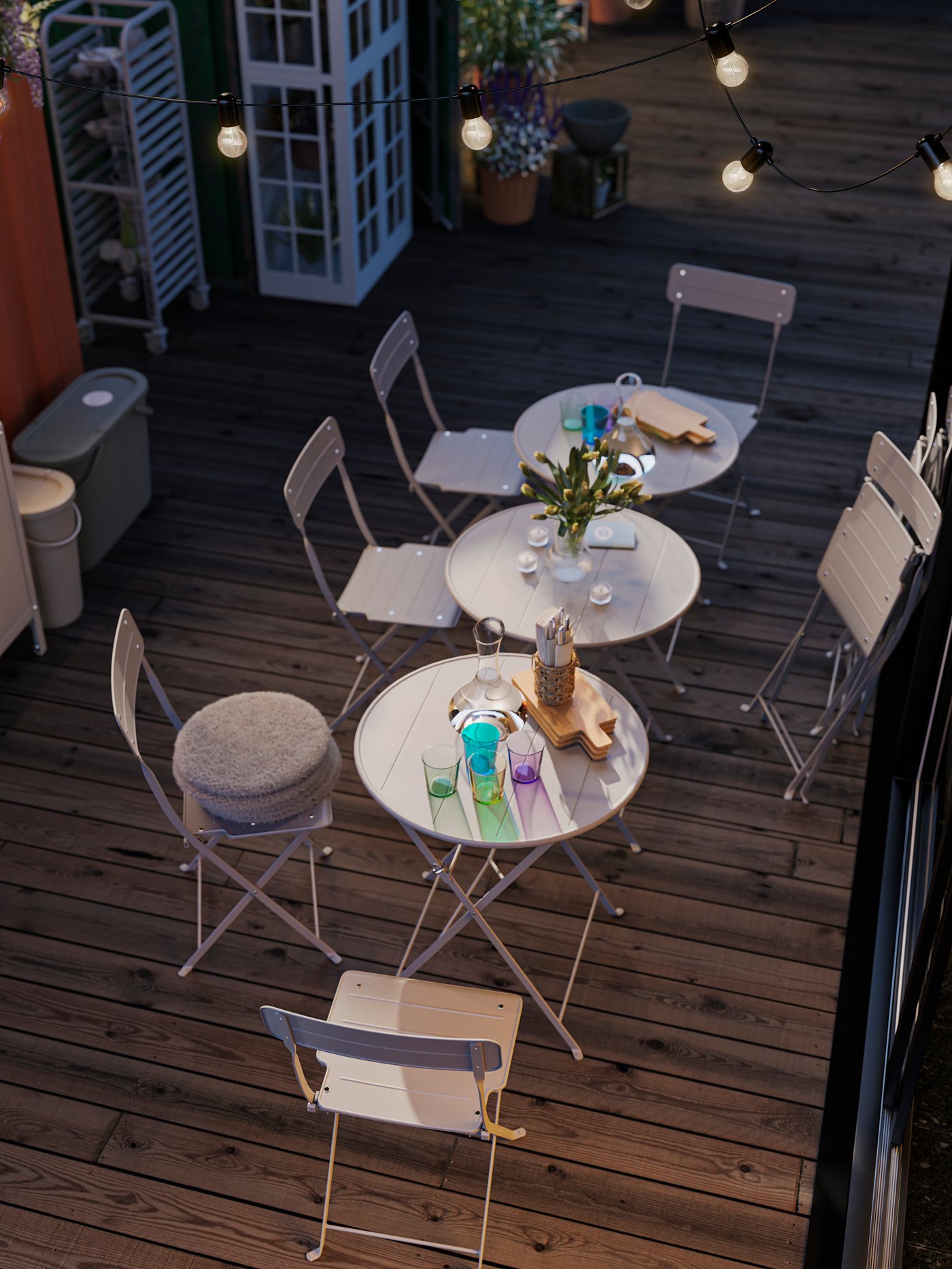 In einem Aussenbereich sind SUNDSÖ Tische und Stühle zu sehen. Auf den Tischen befinden sich Gläser, Karaffen und Schneidebretter.
