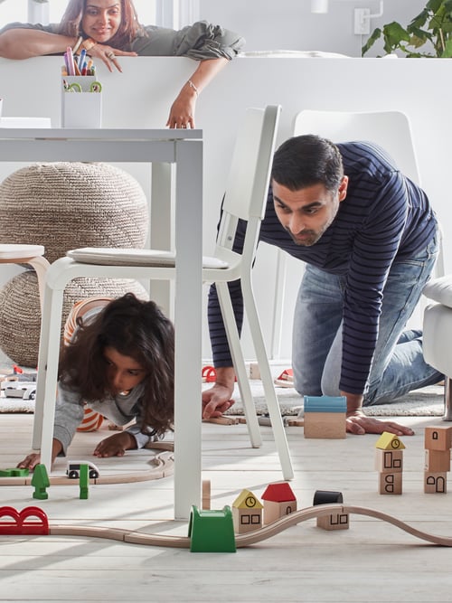 Un père et enfant jouant avec un jeu de train LILLABO qui est en cours d'exécution sous et autour d'une table LANEBERG et des chaises TEODORES.