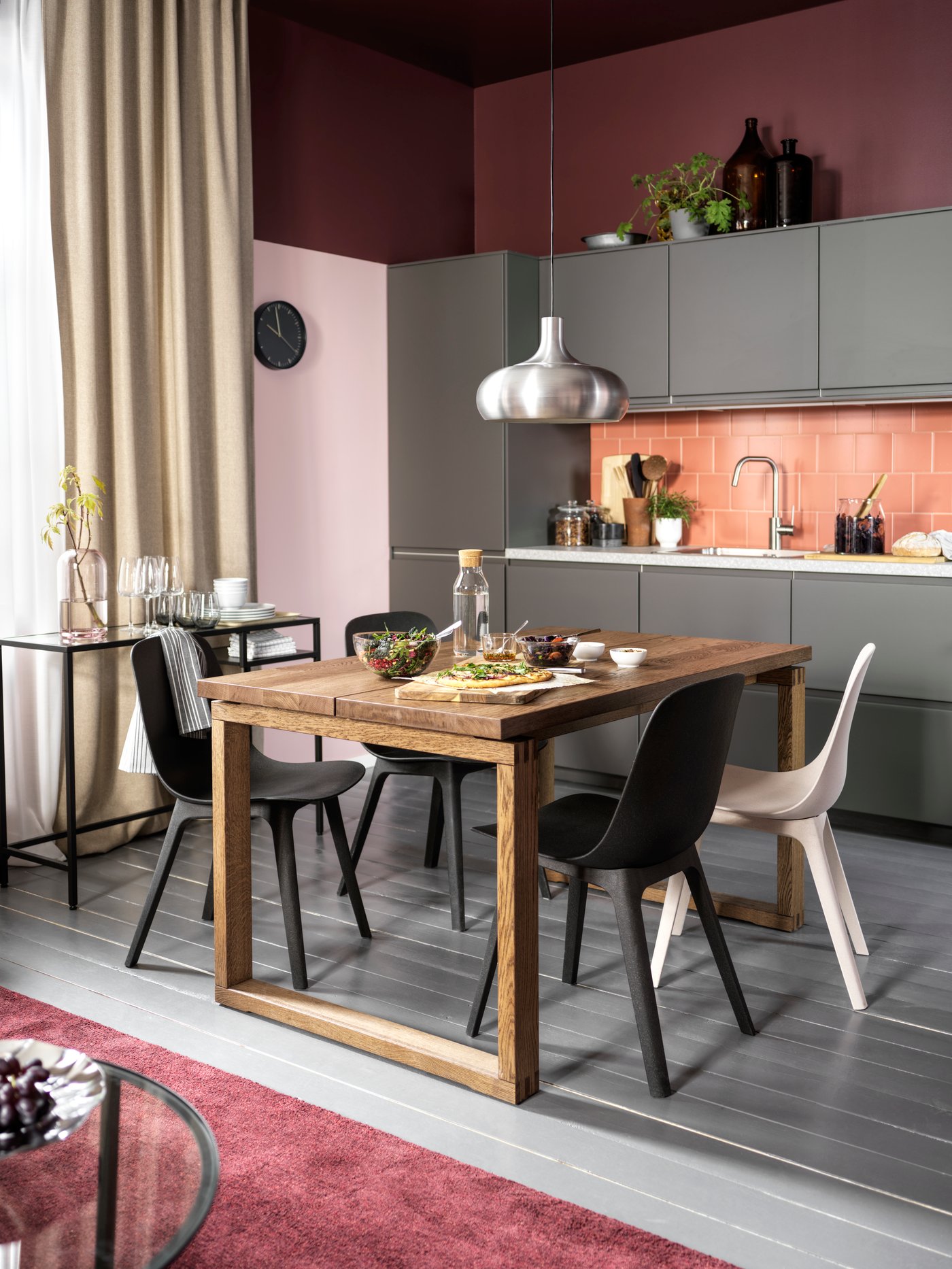 A kitchen with dark grey fronts, a table in oak veneer, chairs in anthracite/white and an aluminium-coloured pendant lamp.
