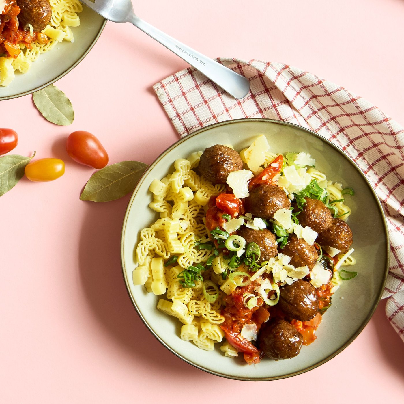 A pale green plate contains a dish of pasta, plant balls and a ragout of tomato and spinach with parmesan and spring onions