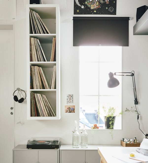 Estante KALLAX blanco junto a una ventana, con discos de vinilo en sus repisas interiores.