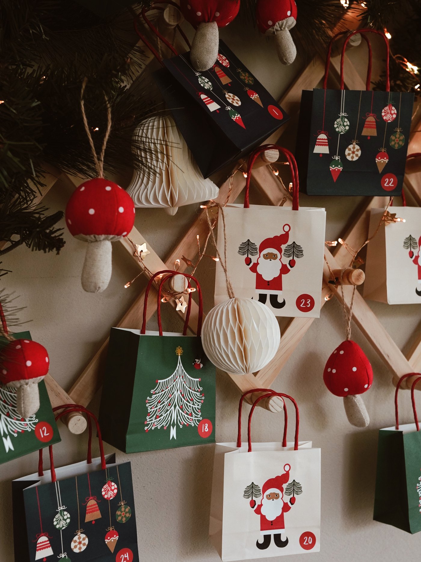 Calendario dell'Avvento natalizio con piccoli sacchetti regalo appesi a una griglia di legno. I sacchetti sono decorati con motivi natalizi, ornamenti e numeri. Atmosfera festosa e accogliente.