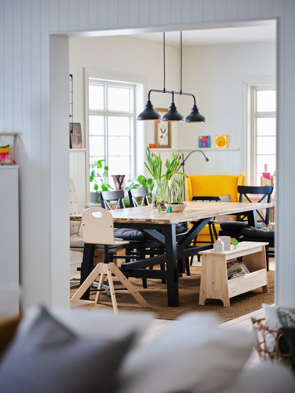 Blick in ein Familienesszimmer mit einem großen Esstisch aus Holz, einer Sitzbank aus Holz mit Stauraum und vielen Stühlen rundherum.