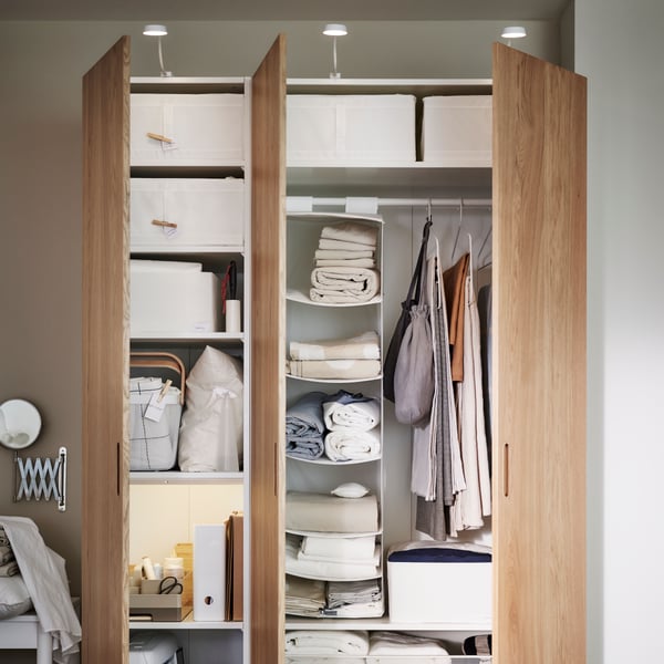A white/oak veneer PAX/TONSTAD wardrobe with both doors open showing SKUBB storage boxes and other items on the shelves.