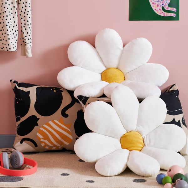 A colourful children’s room corner with toys and headphones on the floor, and two SKOGSDUVA cushions placed on a pillow.