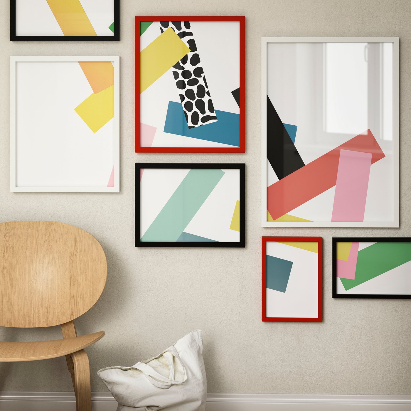 A black RÖDALM frame, next to a red RÖDALM frame and white RÖDALM frame mounted on the wall next to an armchair.
