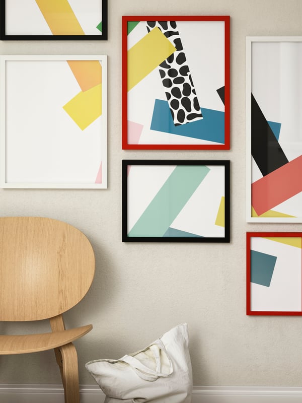 A red, white, and black RÖDALM photo frame on the wall with a wooden chair underneath.