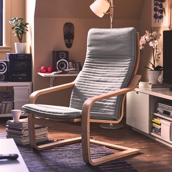 An early 2000s-styled living room has a bentwood frame POÄNG armchair with a light beige cushion by a stack of magazines.
