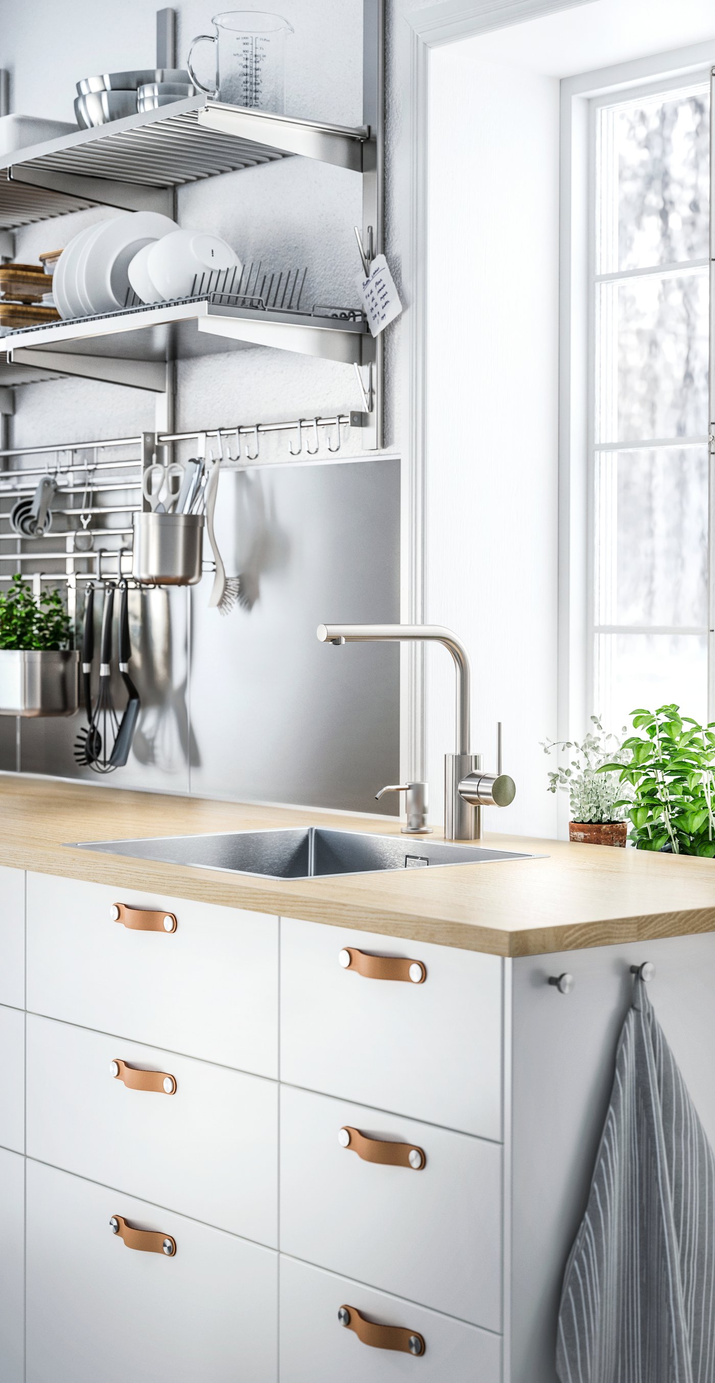 Bílé skříňky s bílými čely zásuvek a koženými úchytkami ÖSTERNÄS pod dřevěnou pracovní deskou s dřezem a baterií.