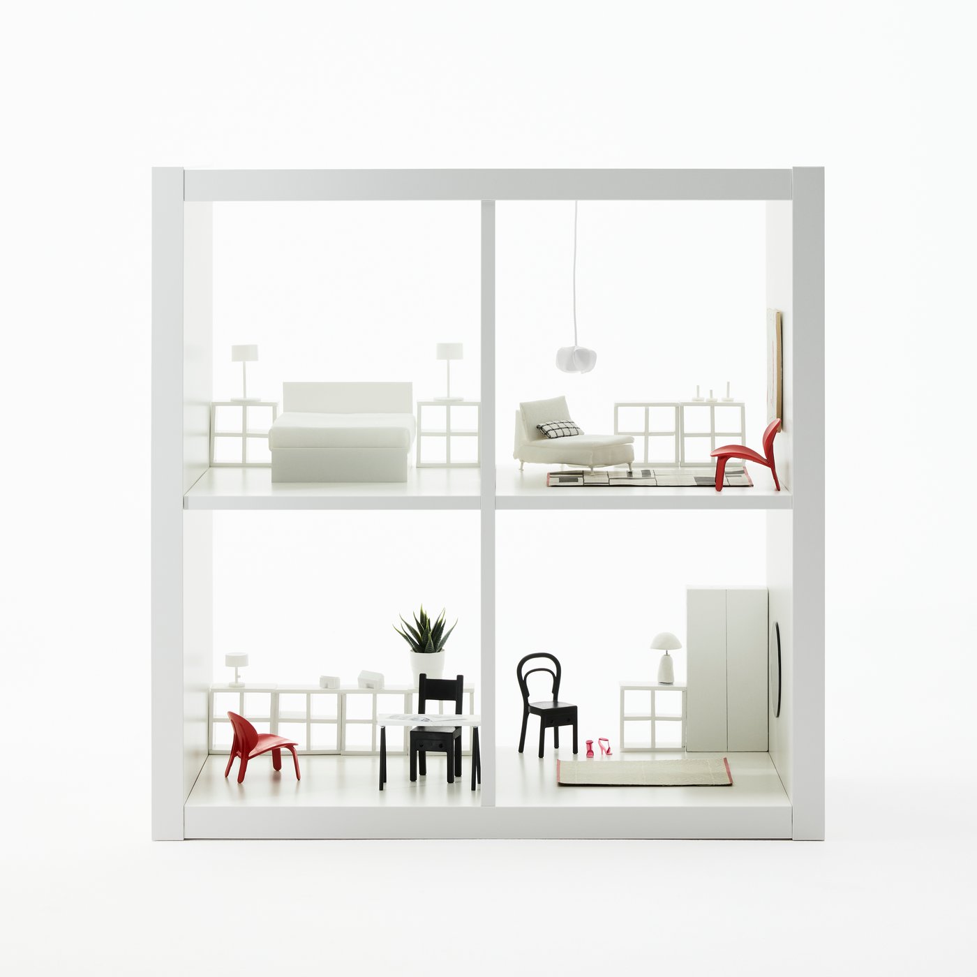 A white KALLAX shelving unit with four shelves. Each shelf has a miniature room set with mini KALLAX and other furniture.