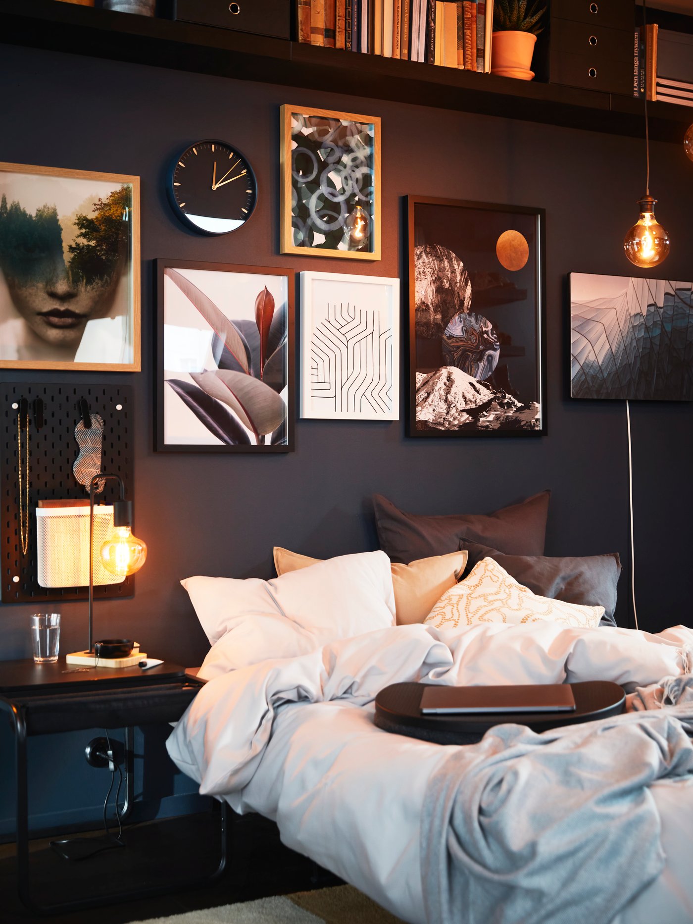 Un lit préparé pour la nuit, une table d'appoint OLSERÖD à côté et un mur décoré d'œuvres d'art avec une enceinte Wi-Fi SYMFONISK avec cadre photo au-dessus.