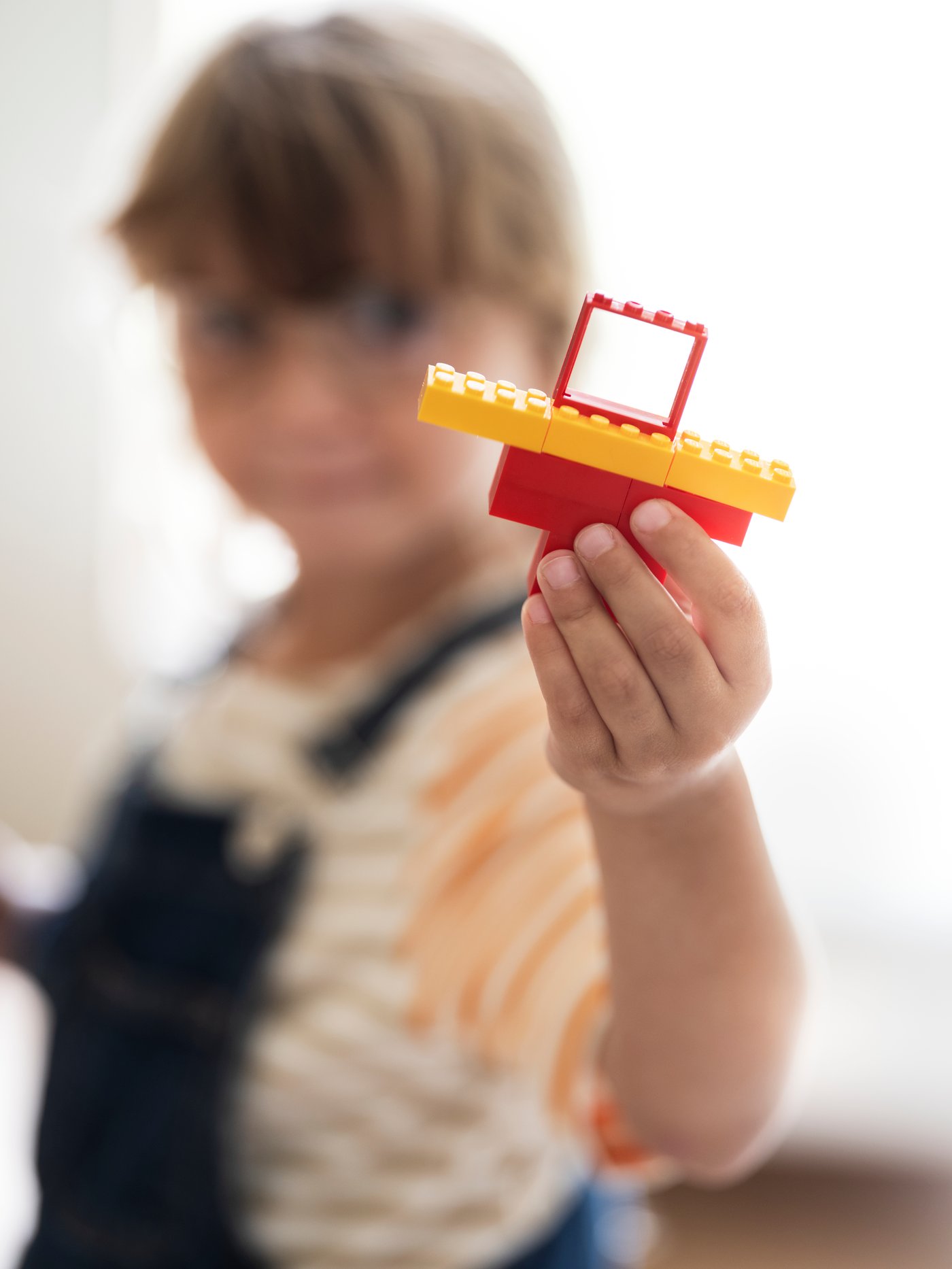 A child stands and holds up a piece of a toy house made out of parts from the BYGGLEK 201-piece LEGO® brick set.