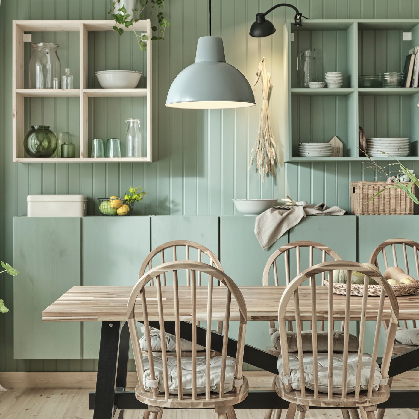 Ein SKOGSTA Esstisch aus Holz und passende SKOGSTA Stühle stehen in einem Esszimmer vor grün gestrichenen IVAR Schränken.