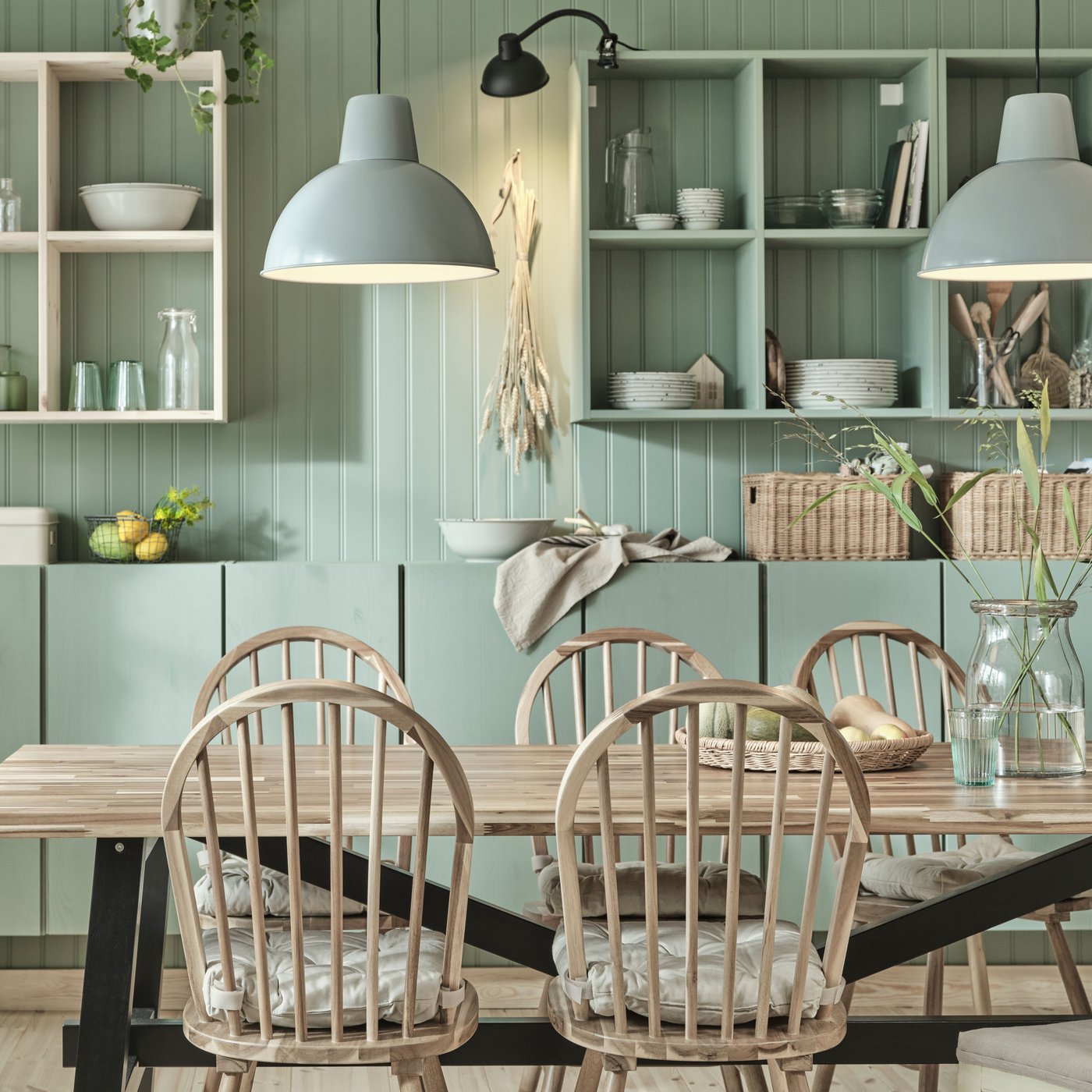 A wooden SKOGSTA dining table and matching SKOGSTA chairs stand in a dining room in front of green-painted IVAR cabinets.