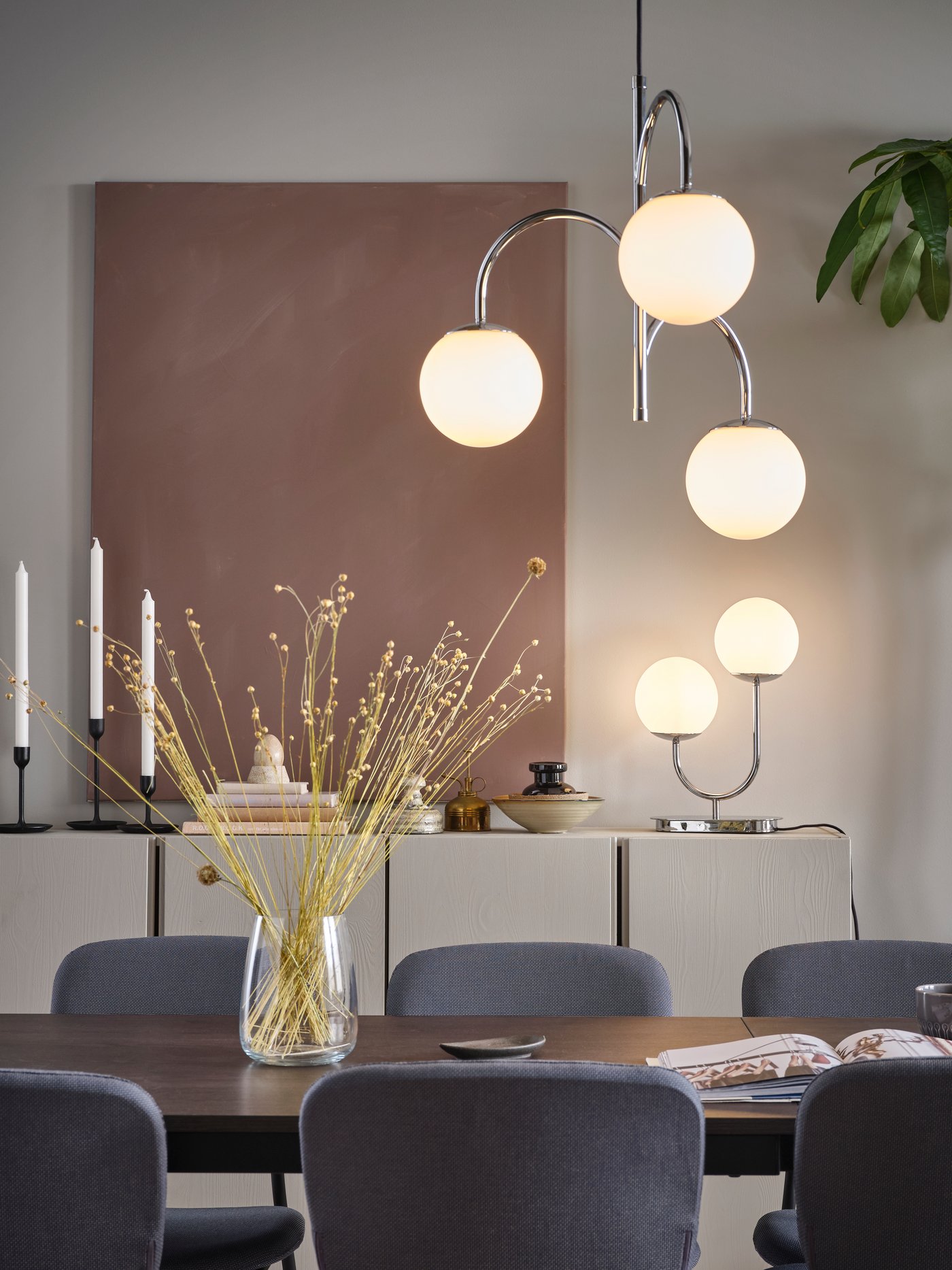 En SIMRISHAMN bordslampa och en SIMRISHAMN taklampa i förkromat/opalvitt glas i en matsal.
