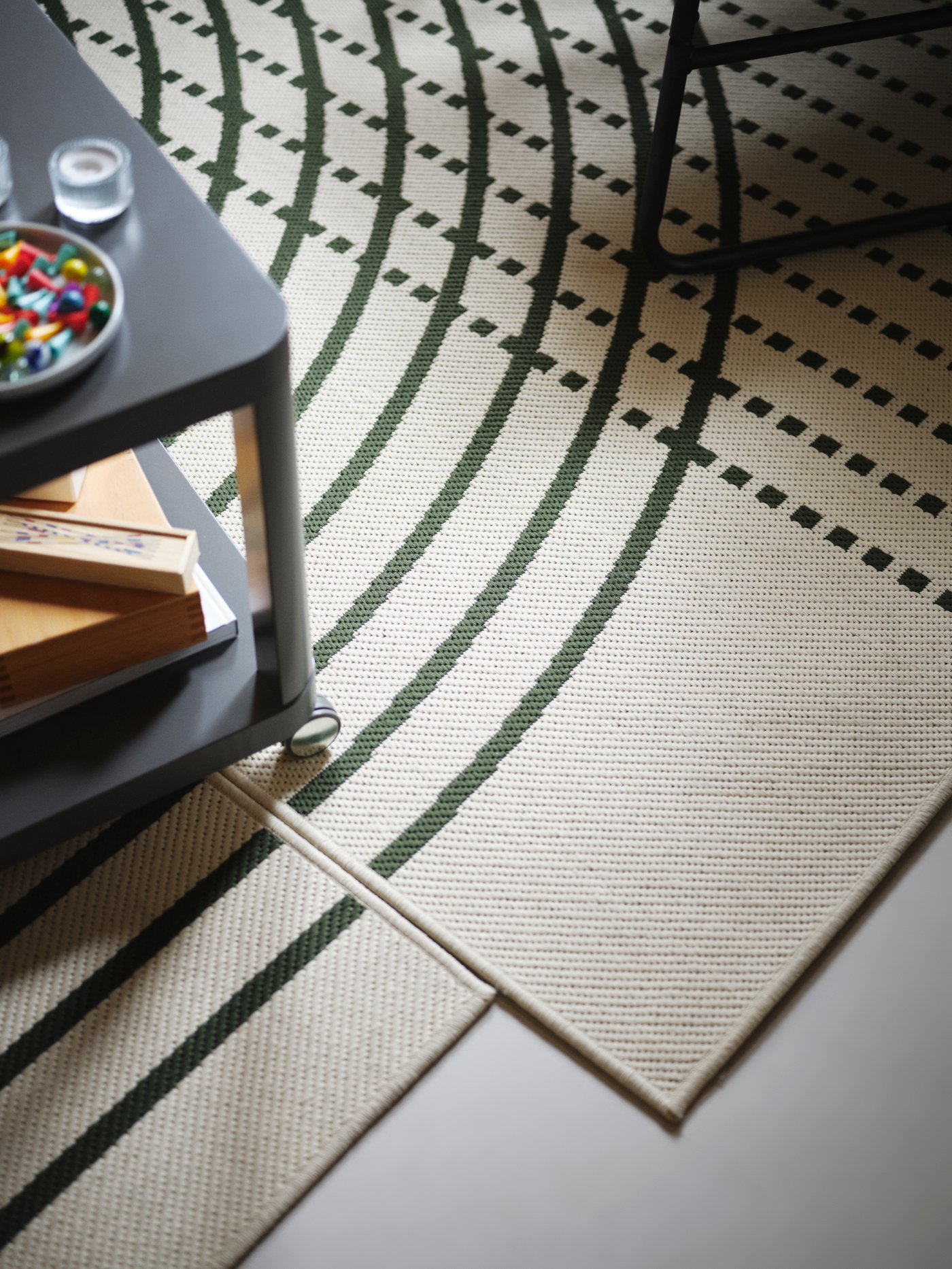 A grey TINGBY side table with various items on top, on two dark green/off-white TÖMMERBY flatwoven rugs.