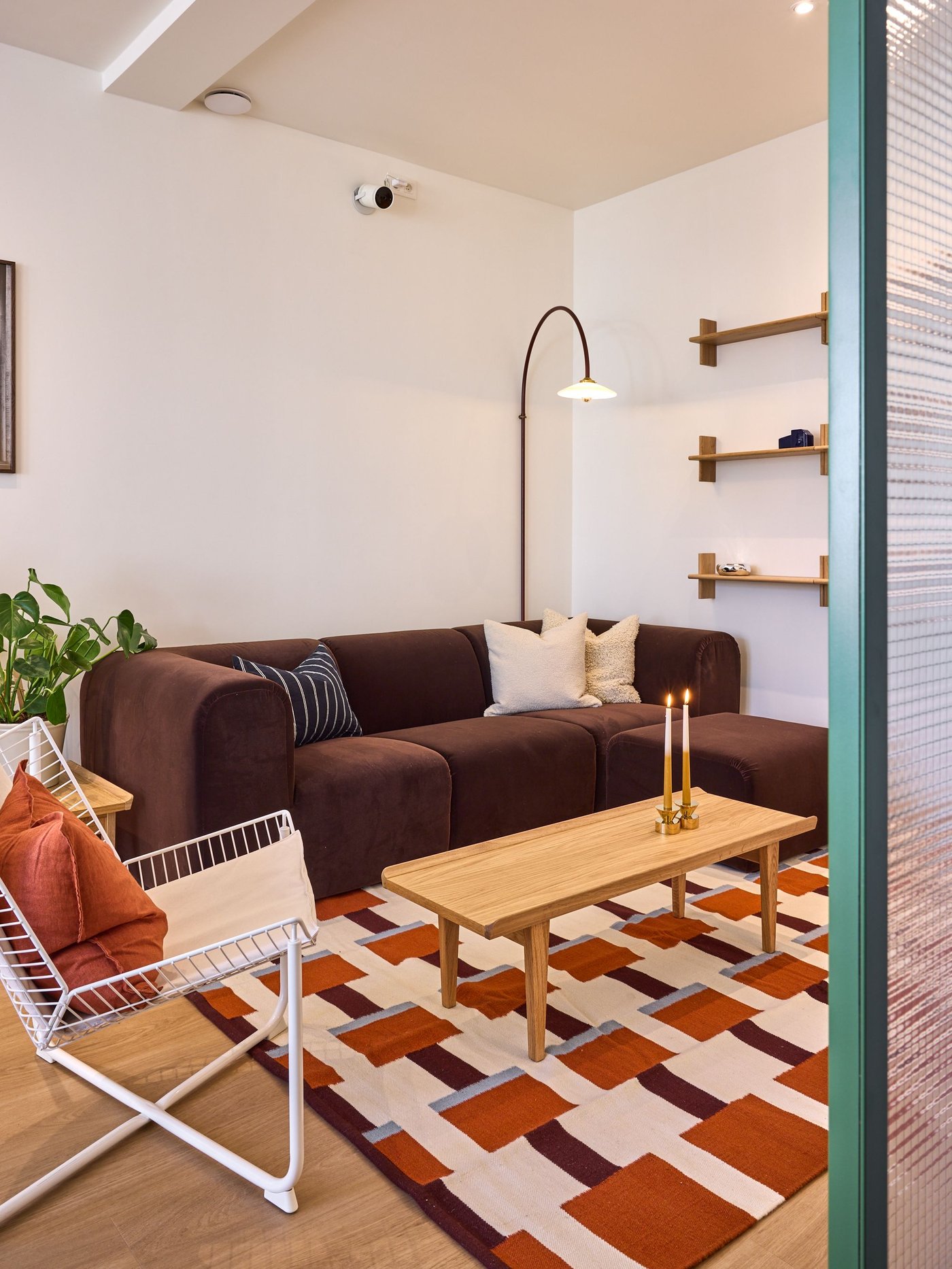 Gezellige woonkamer met bruine zetel, houten salontafel, wandplanken en grafisch tapijt in warme tinten.