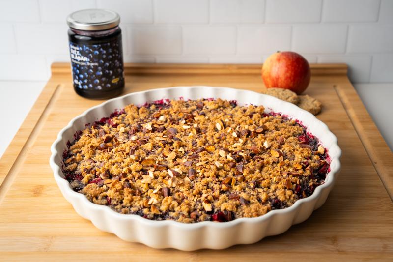Apfel-Blaubeer Crumble in einer Auflaufform auf einem Schneidebrett präsentiert.