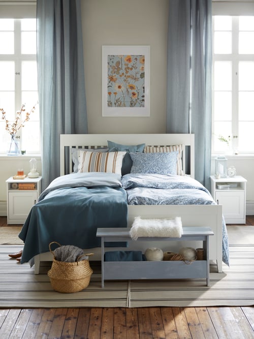 Bedroom area with a bed frame with storage, with multiple pillows, a duvet cover, nightstand, basket, a bench, and a rug.