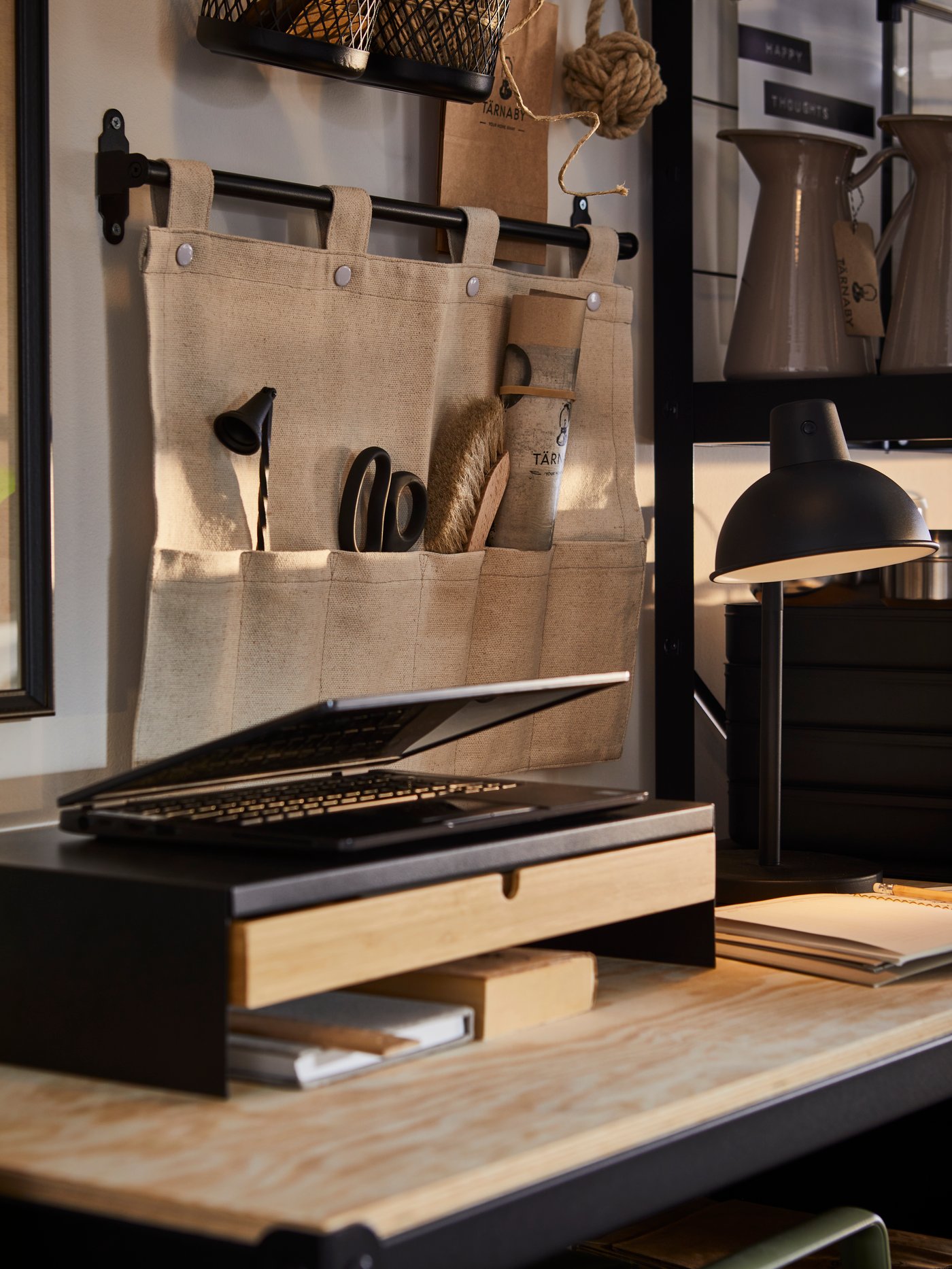 A NEREBY hanging organiser for accessories hangs on a wall above a work bench with a monitor stand and a work lamp on it.