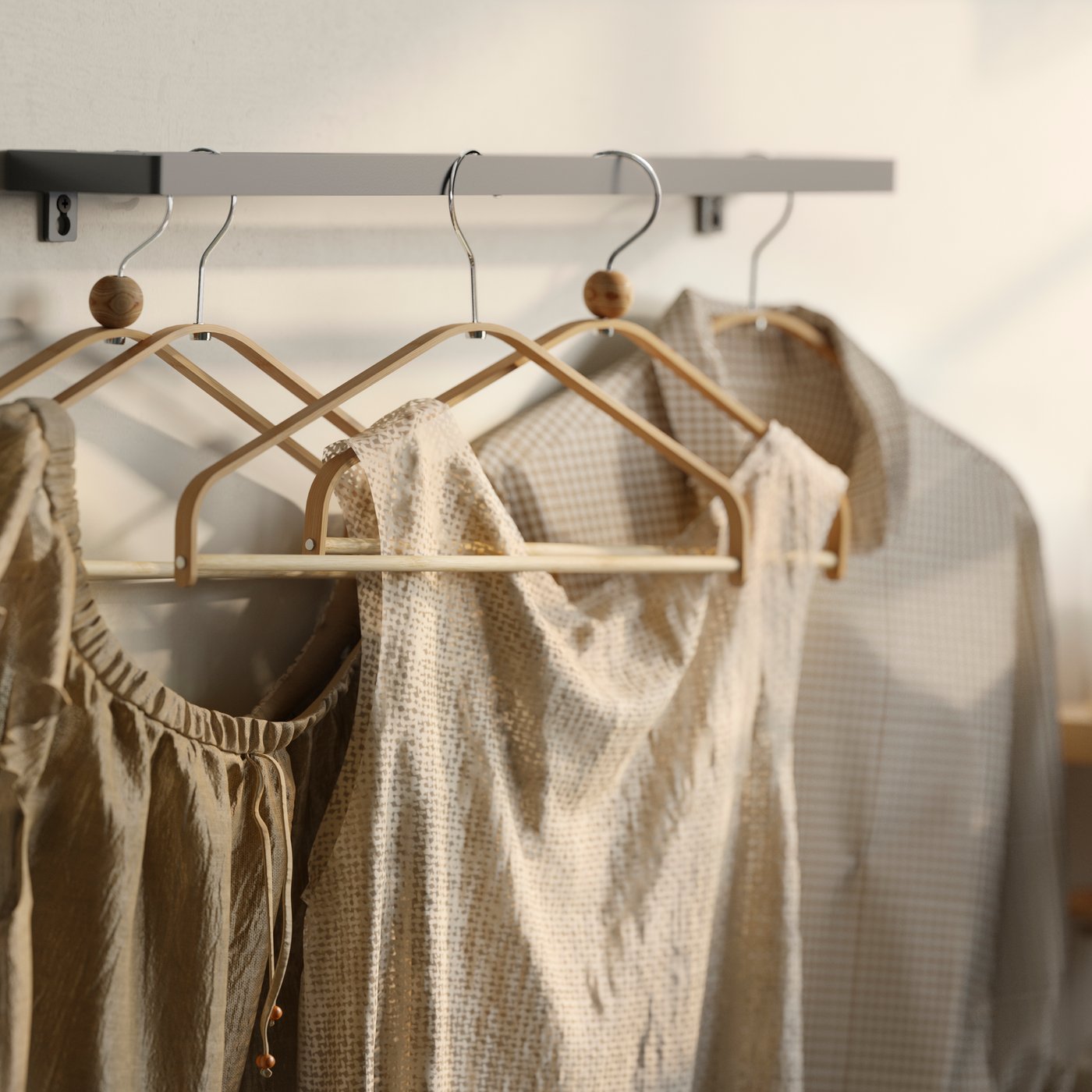 Flera HÖSVANS galgar i bambu på en väggmonterad metallskena, med beigefärgade skjortor och klänningar bredvid ett bord.