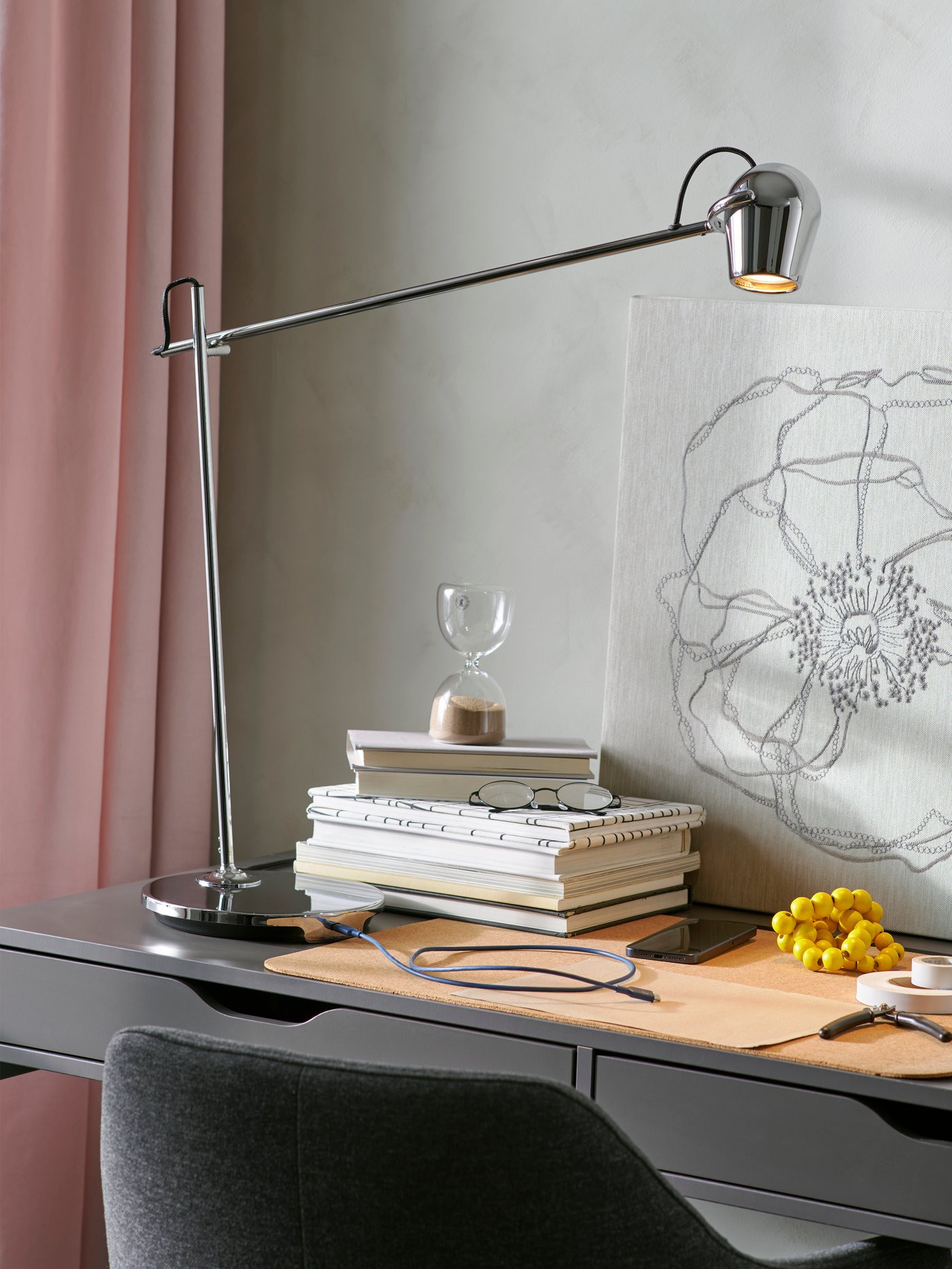 En kromad MODERMOLN arbetslampa står på ett skrivbord med en kontakt ansluten till dess inbyggda USB-C-laddningsport i lampans fot.