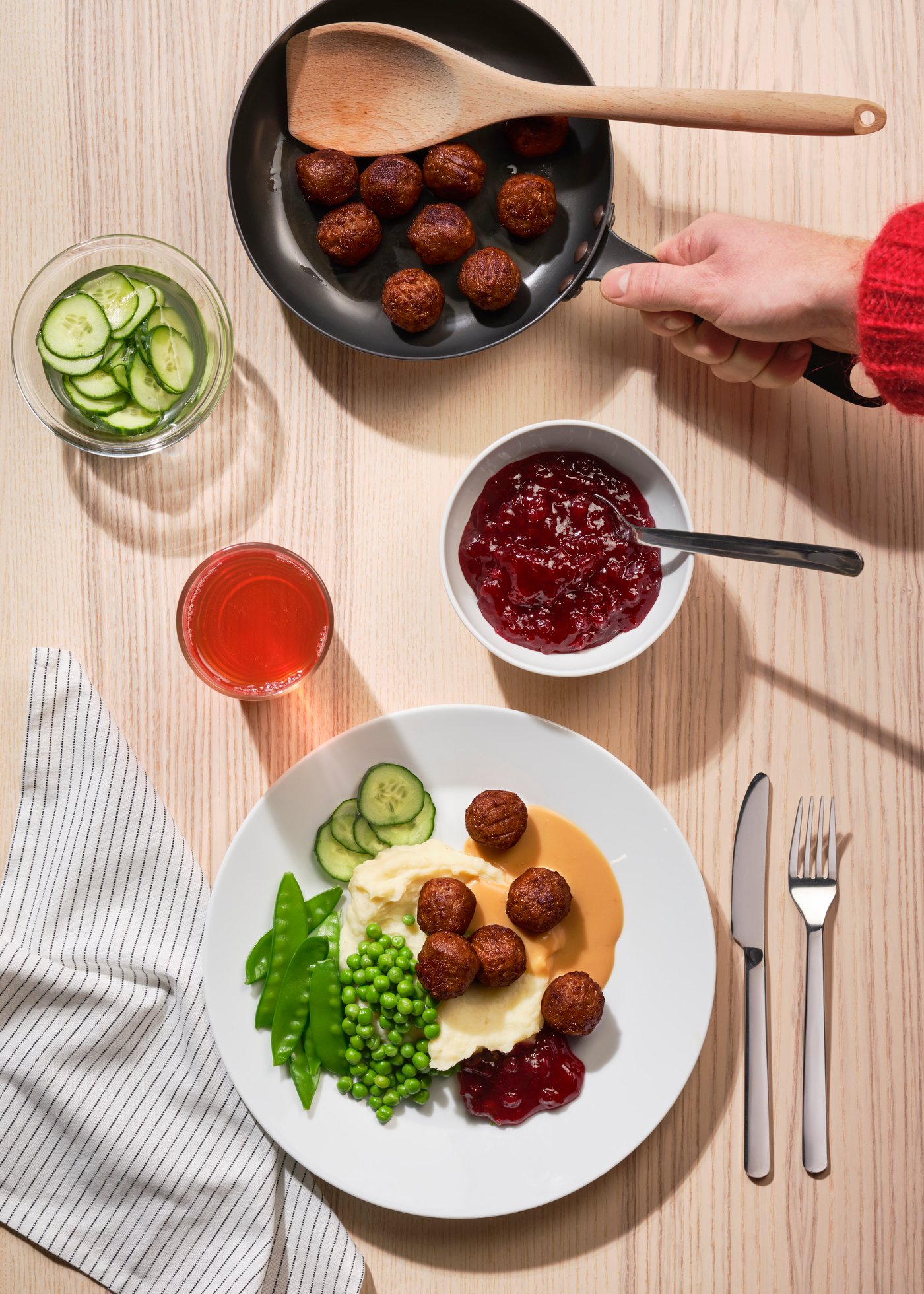 Une table sur laquelle sont posées une poêle contenant des boulettes de viande, et une assiette accueillant des boulettes, de la purée de pommes de terre et des pois. 