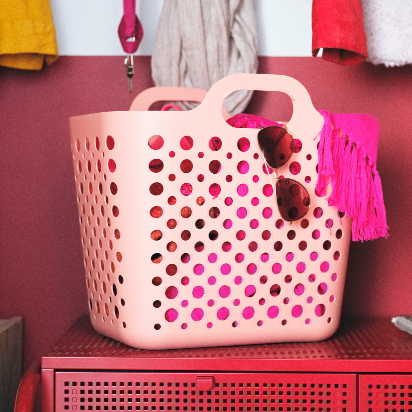 A pink SLIBB flexible laundry basket holding accessories stands on a red NIKKEBY four-drawer chest of drawers.