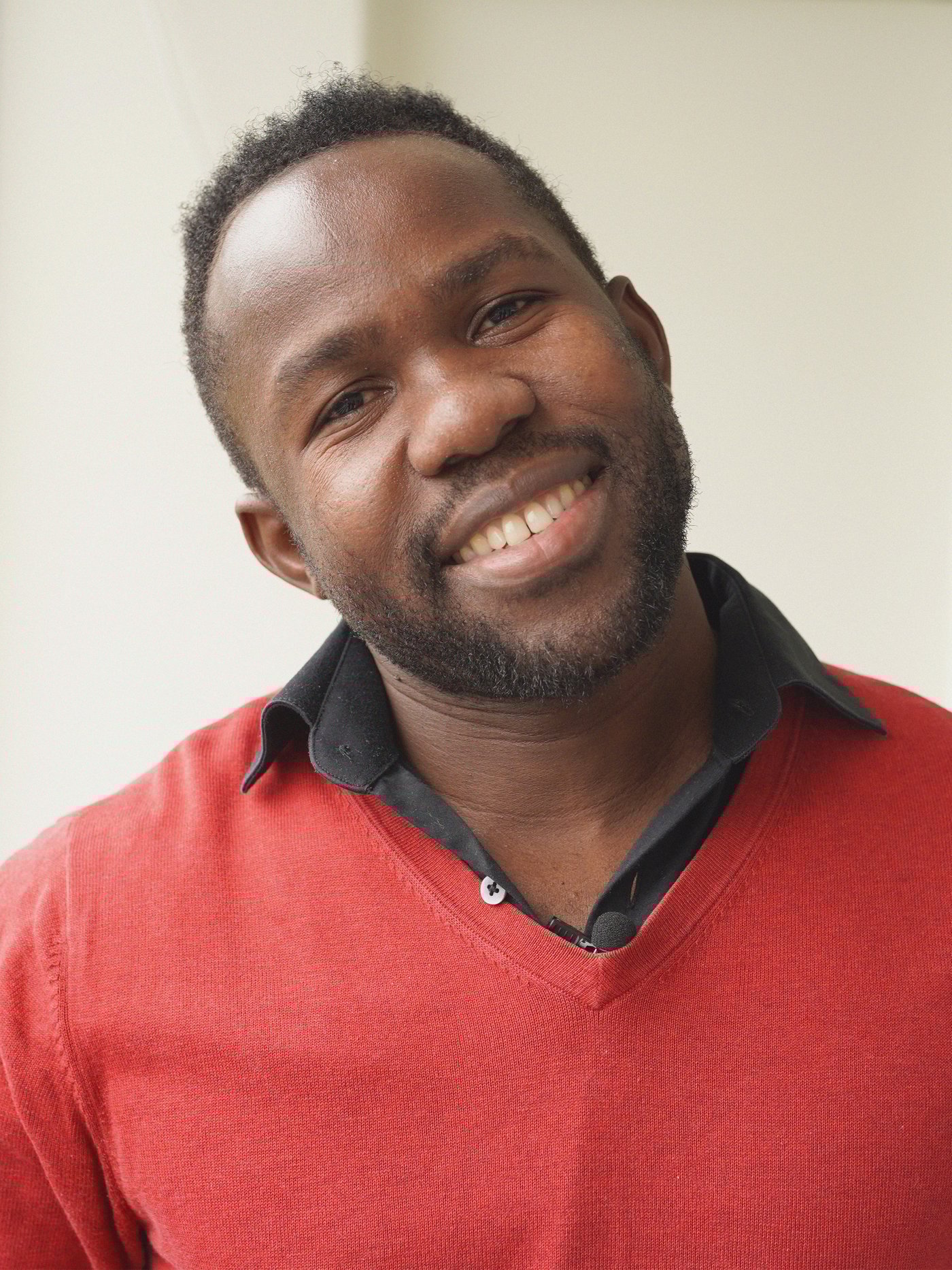 a man smiles at the camera on his balcony in a red sweater.